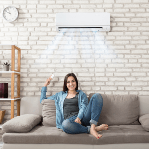 woman sat on sofa underneath an air conditioning unit with remote in her hand